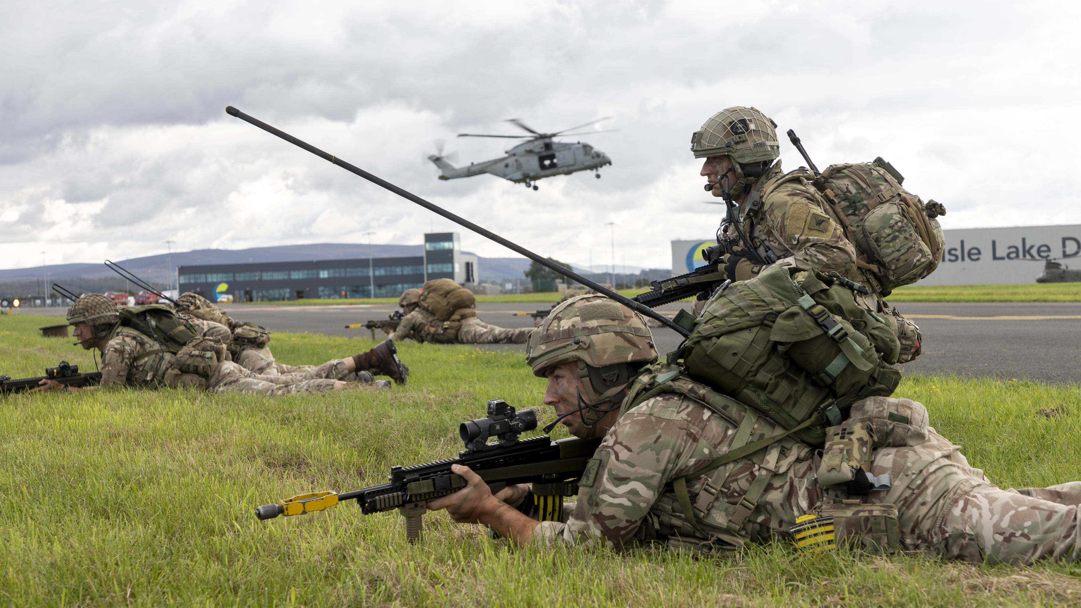 Image shows RAF personnel with rifles, moving in prone on an airfield.